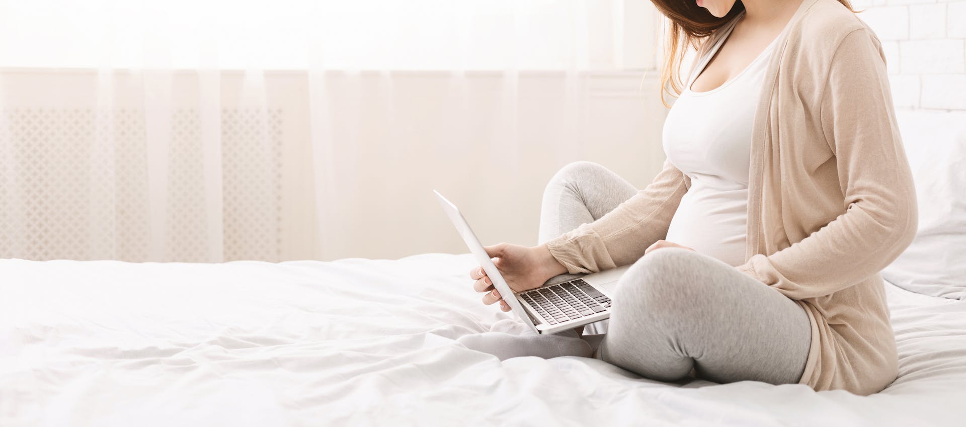 pregnant mother reading from the laptop on the bed