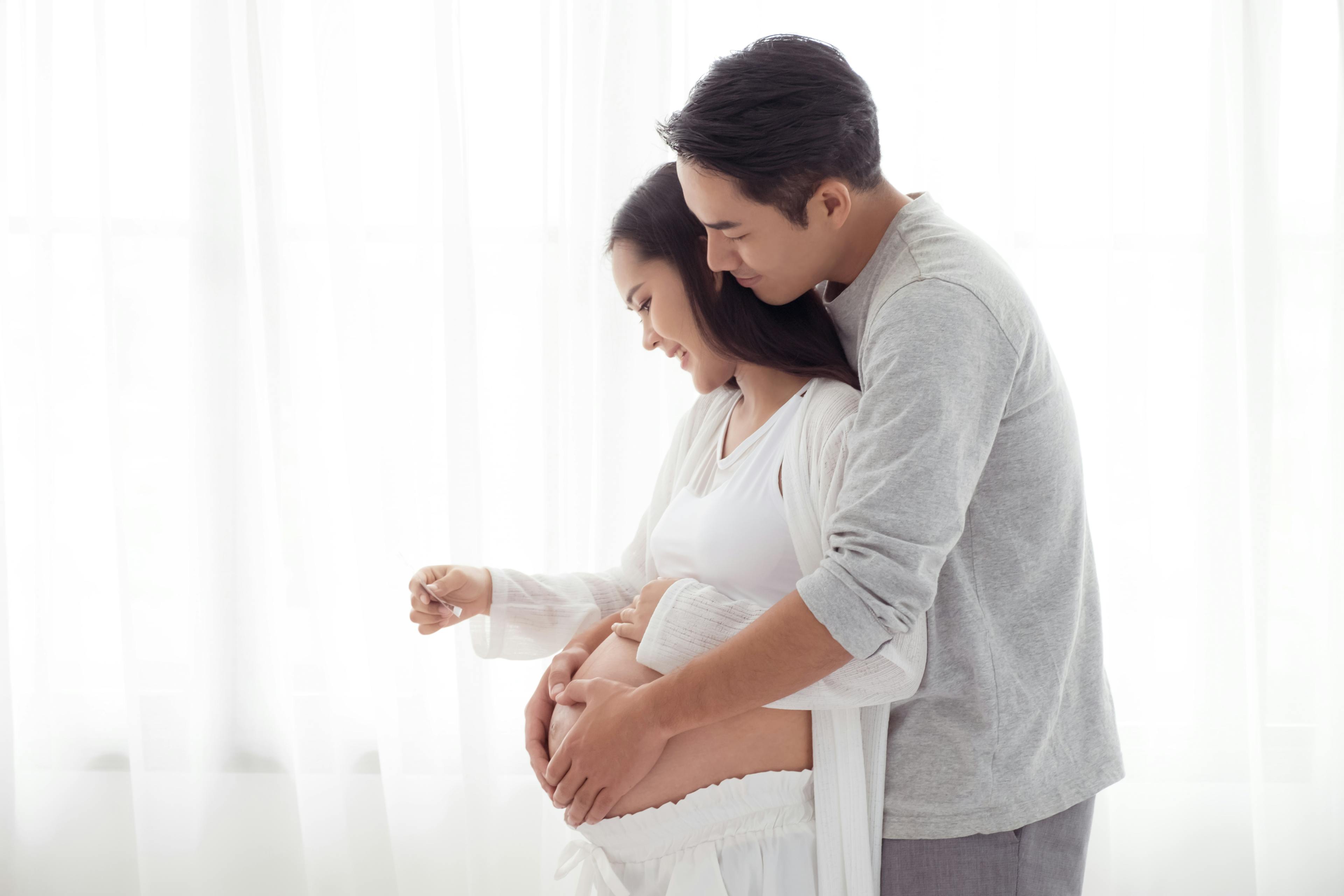 Young Asian couple pregnant and cradling stomach